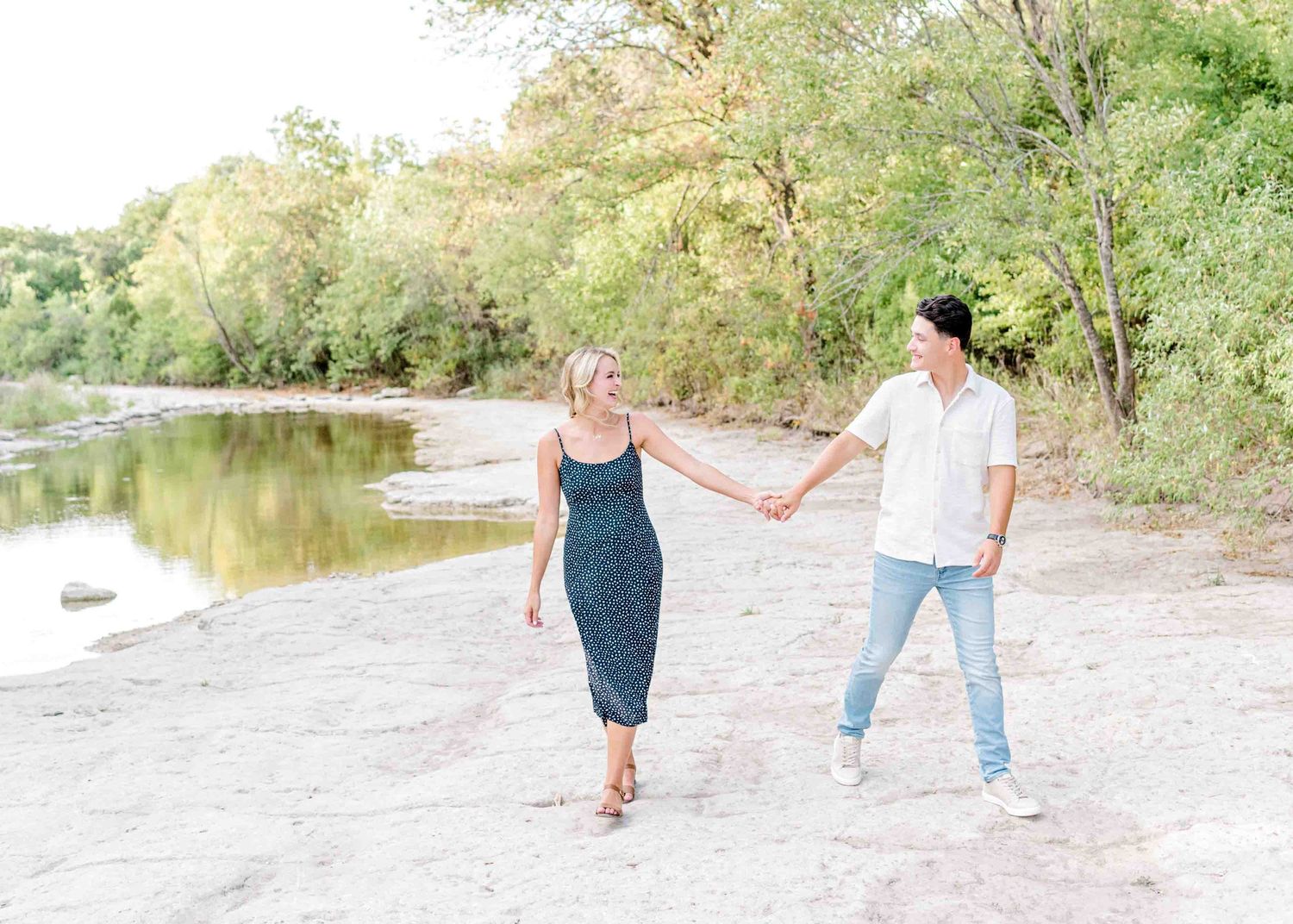 Couple holding hands while walking along a serene waterfront path surrounded by nature.