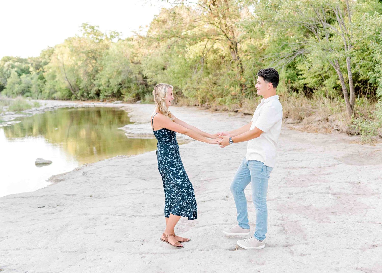 Dancing couple enjoying a romantic moment by the water's edge in casual attire.