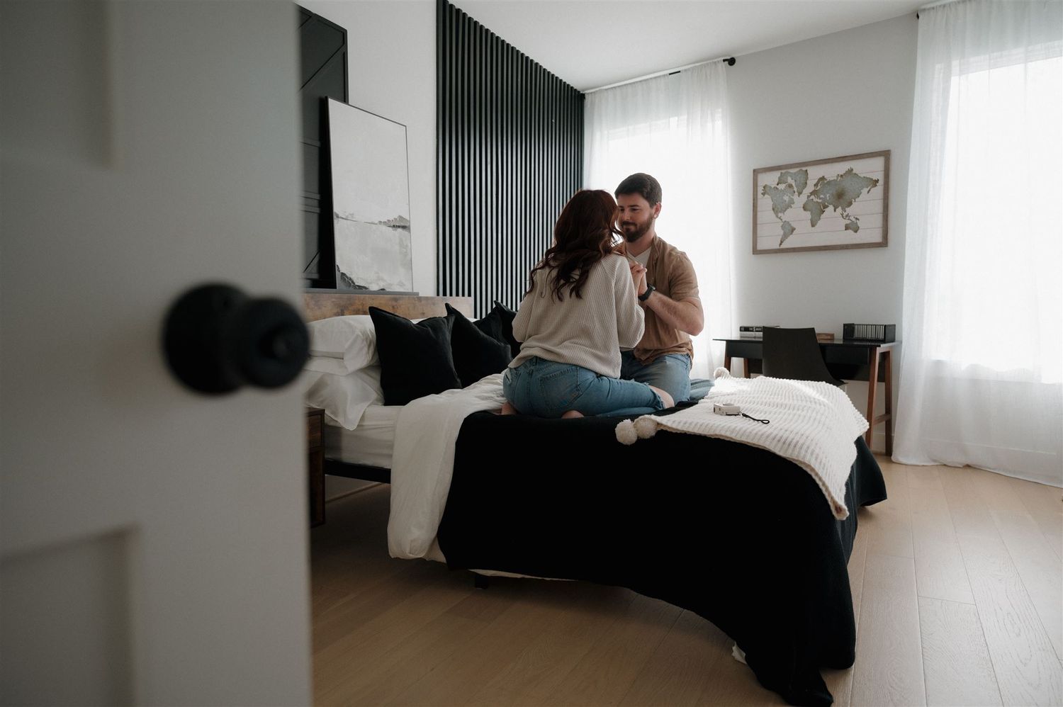 A playful couple laughing together on a bed with black and white bedding.
