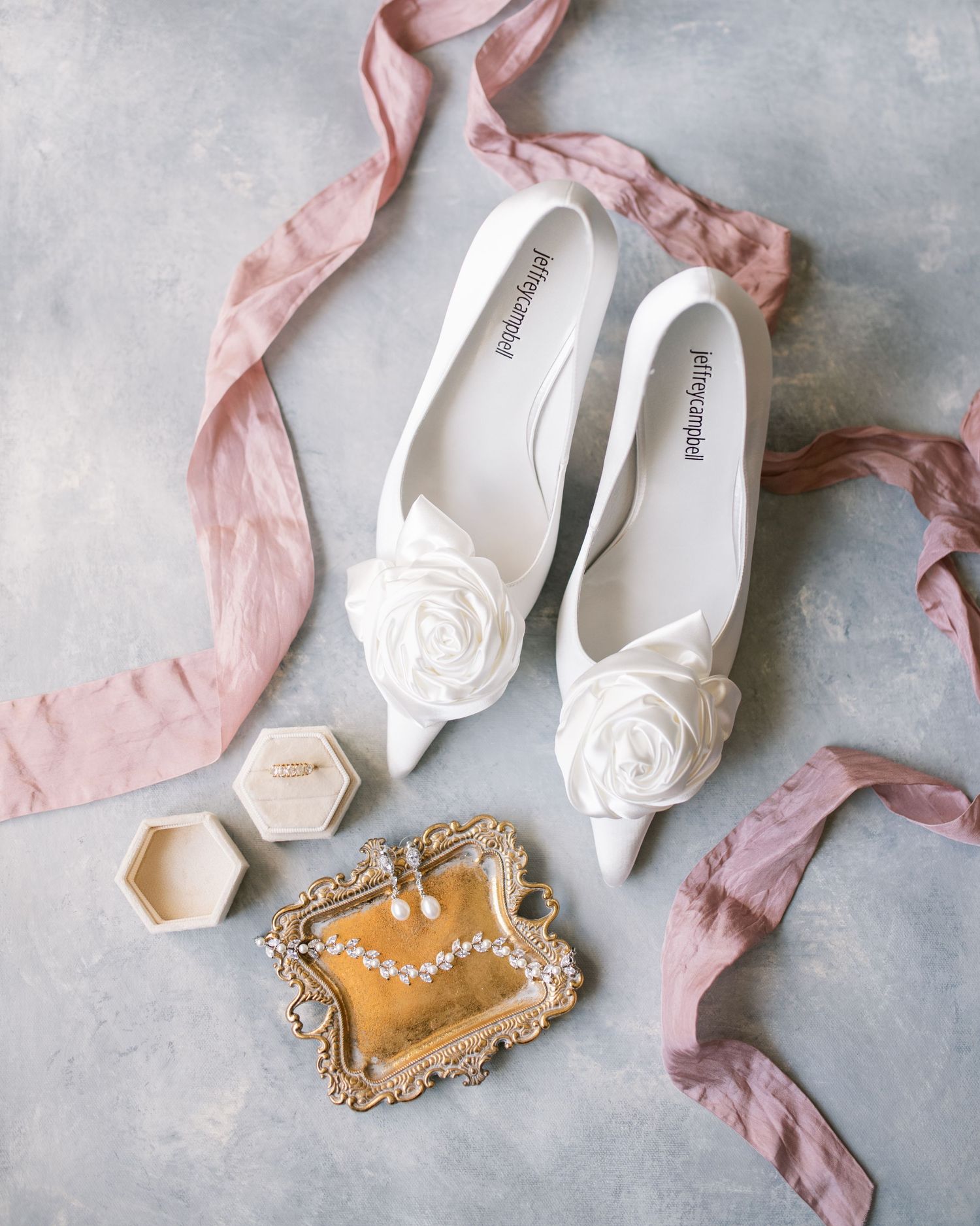 Elegant white bridal flats with rose details alongside pink ribbons and jewelry box.