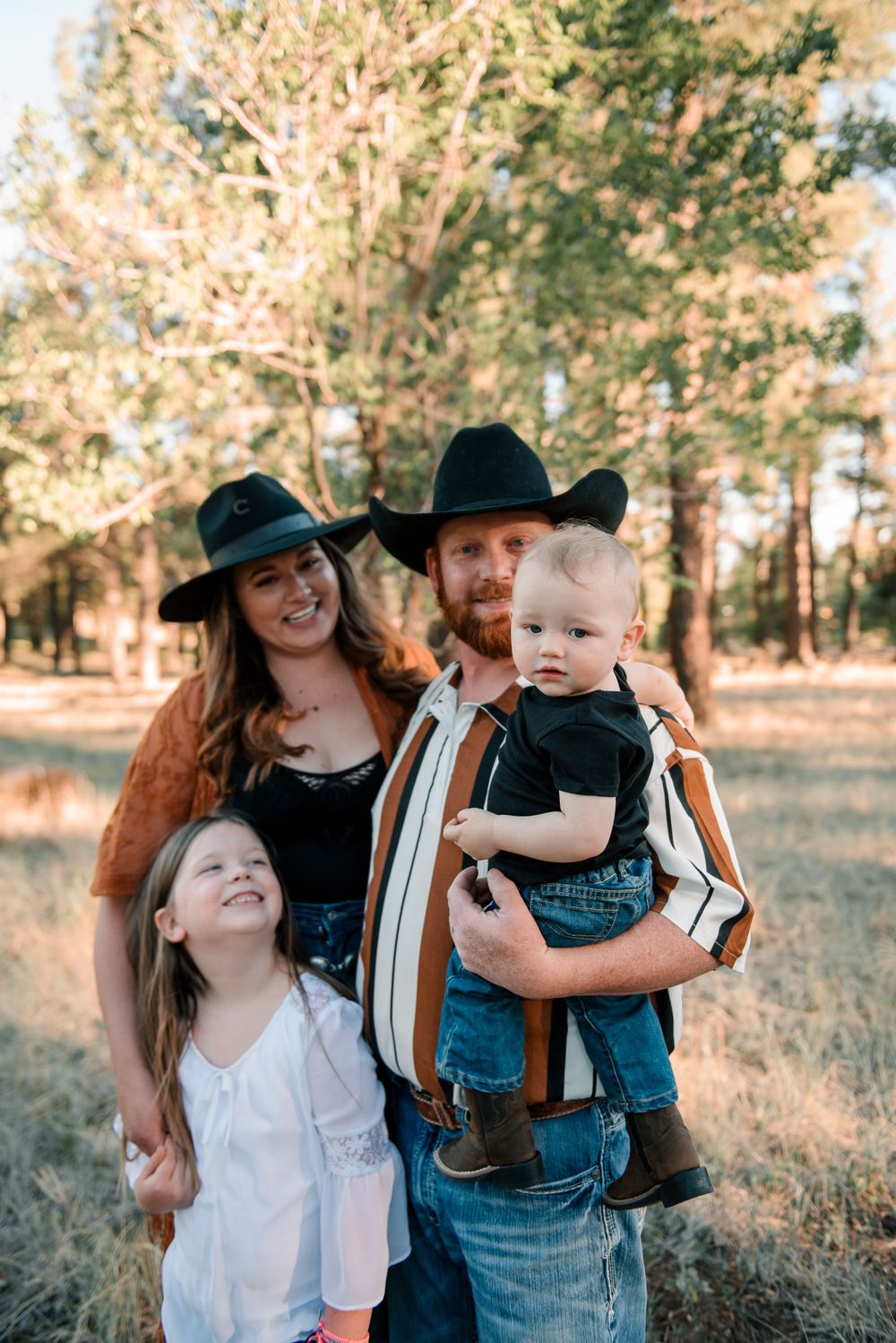 Family in western attire enjoying outdoor photoshoot among pine trees at sunset.
