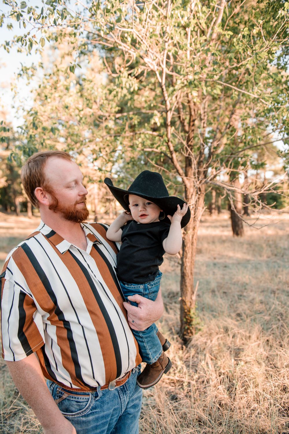 Father and child sharing tender moment in outdoor setting wearing western attire.
