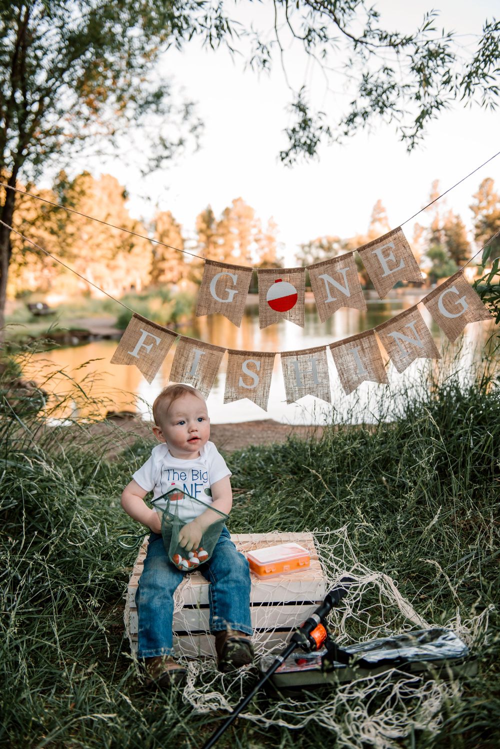 Child smiles while holding orange bobber with rustic banner decorations in outdoor setting.
