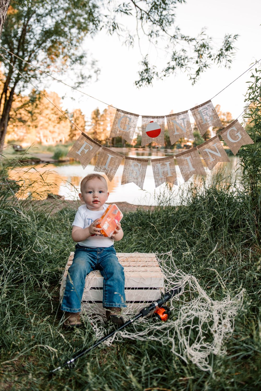 Young fisher sits on wooden platform with orange fishing float and decorative banners.