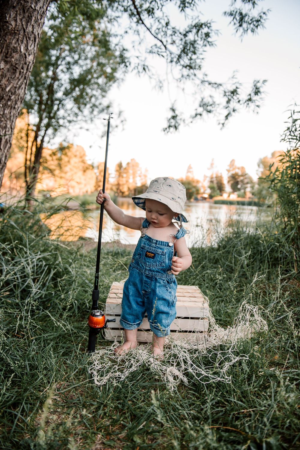 Small child practices casting fishing rod in natural outdoor setting.