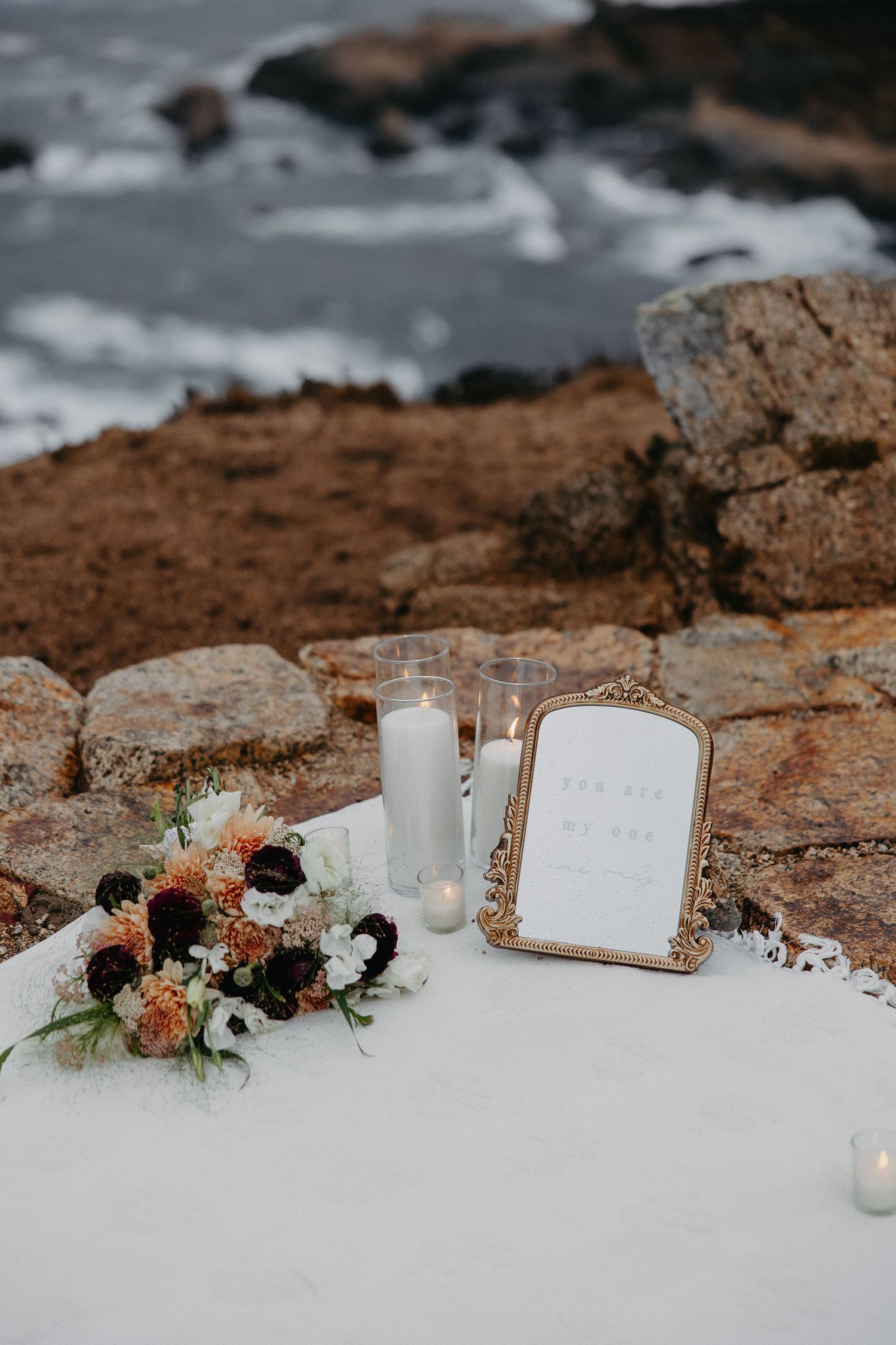 White candles and floral arrangements set up on rocky coastal cliffs for a romantic occasion.