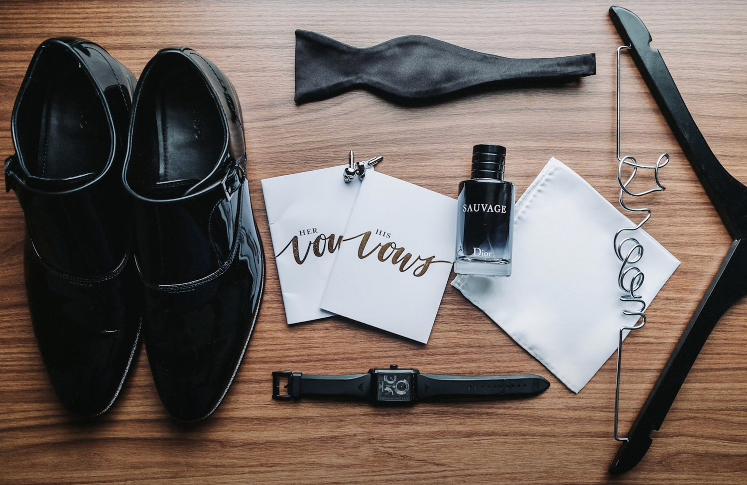 Black formal shoes with watch, fountain pen, and writing accessories on wooden surface.