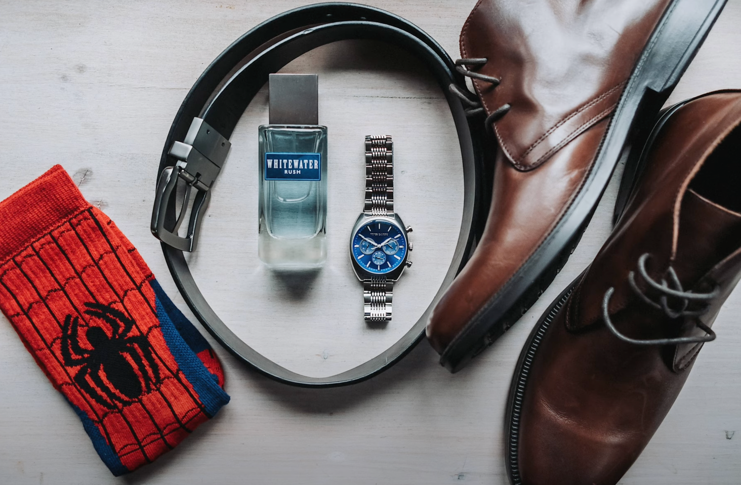 Brown leather boots with headphones, watch, and Spider-Man socks arranged on white surface.