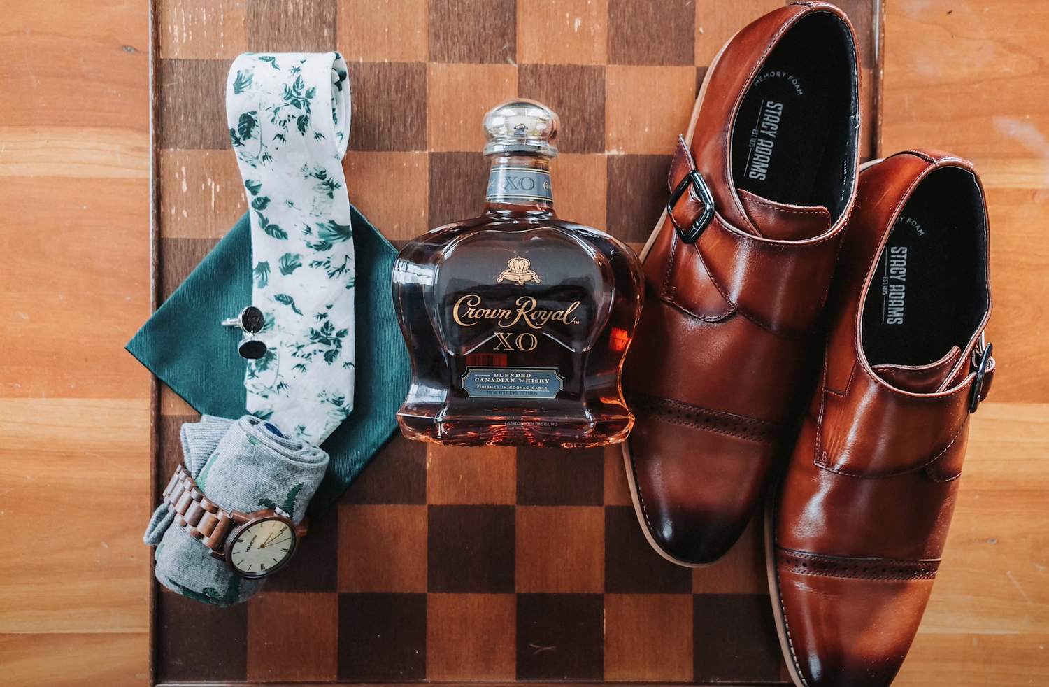 Brown leather monk strap shoes with Crown Royal whiskey and floral tie on a chess board background.