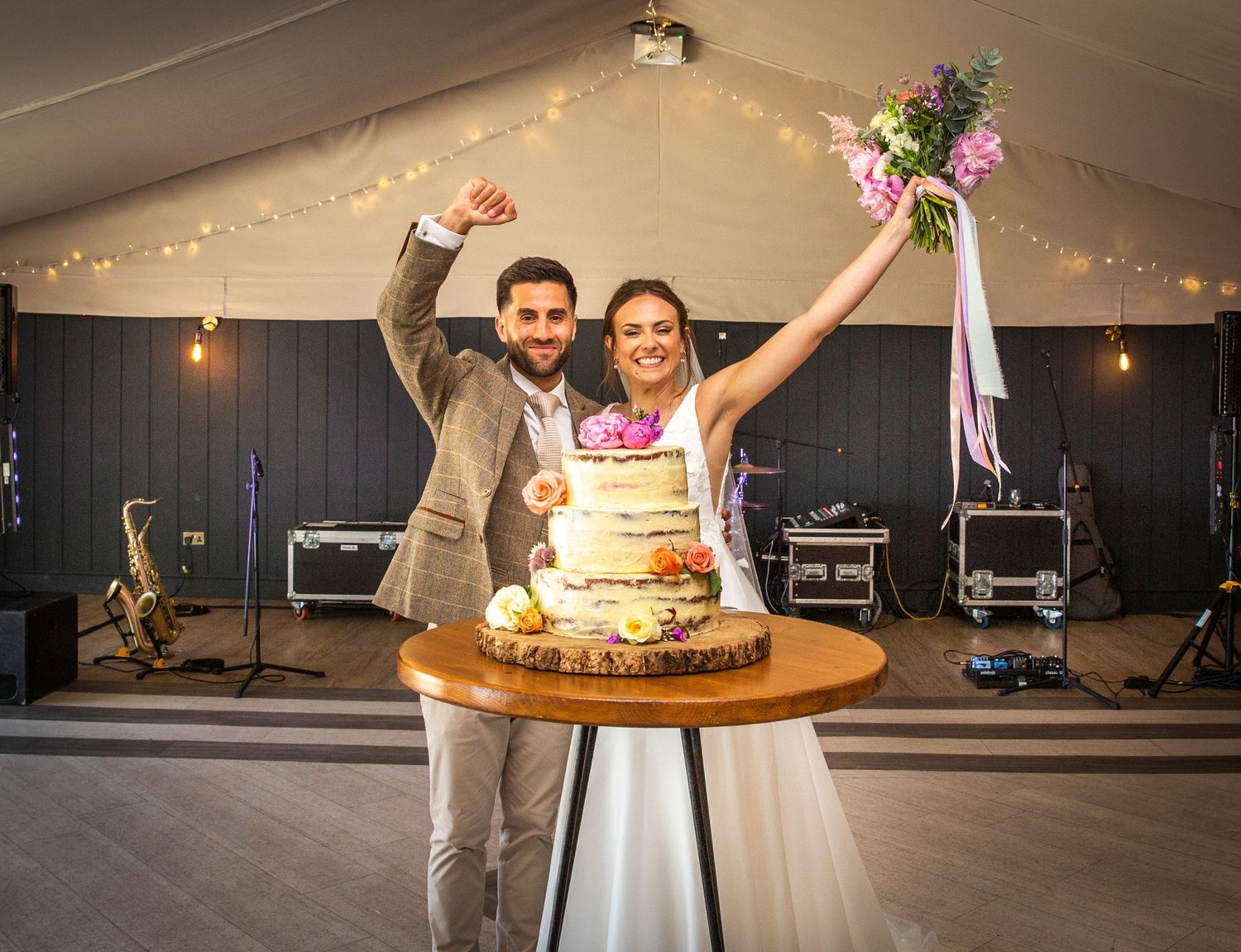 Wedding reception setup inside a tent with wooden tables and string lights.