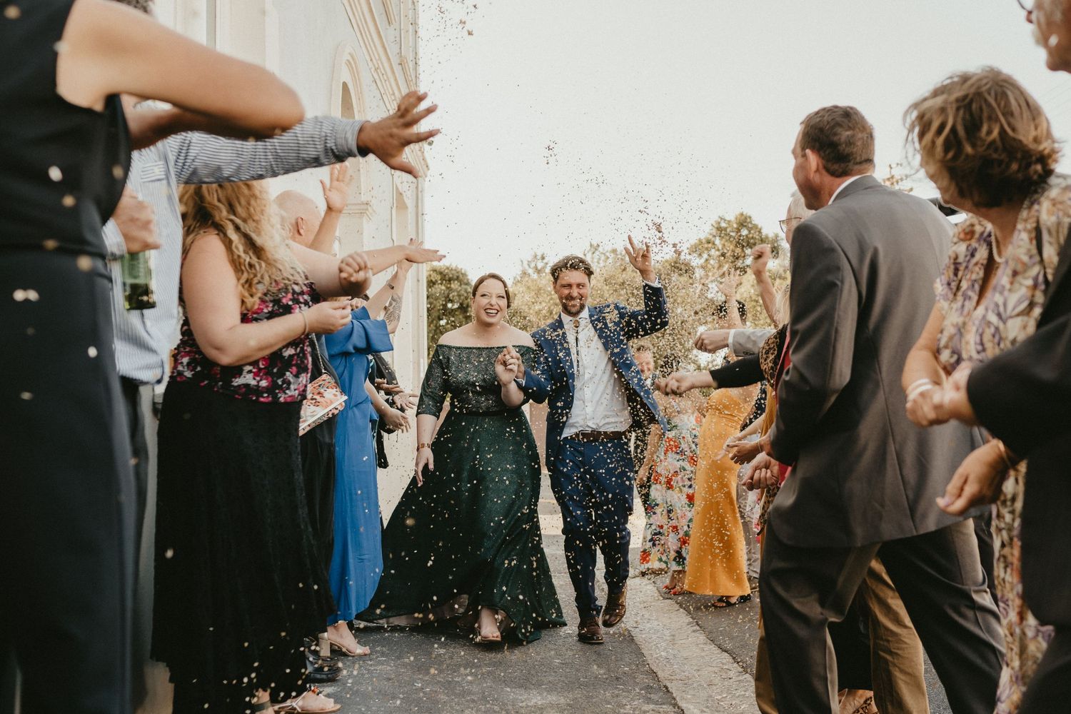 Joyful couple walks through shower of confetti surrounded by wedding guests.
