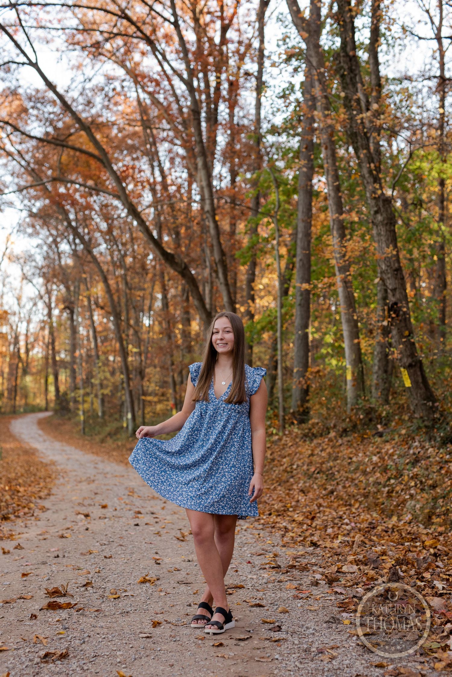 A flowy blue dress being showcased against a backdrop of fall foliage on a forest trail.