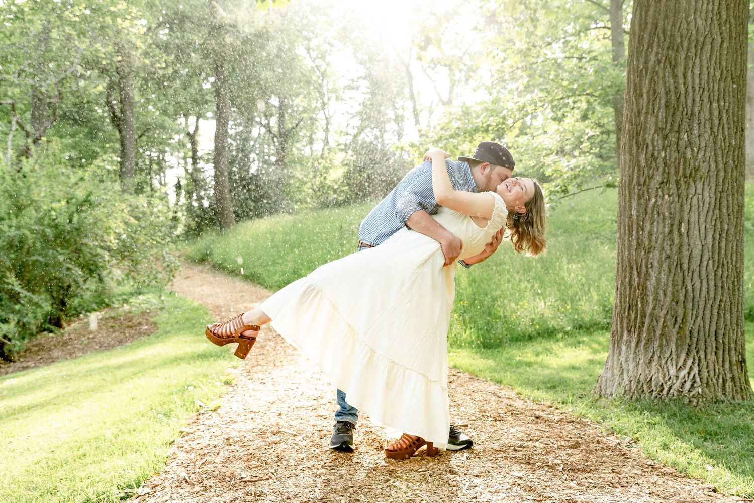 man in blue shirt dipping woman in white dress in the park during golden hour and rainy photography session