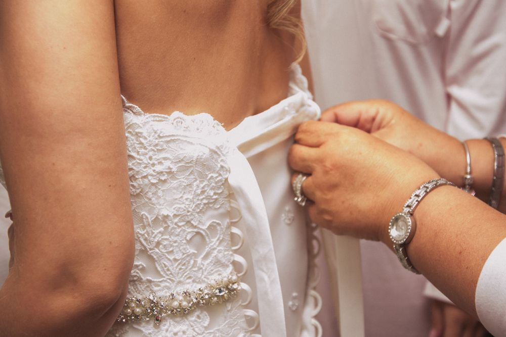 Close-up of hands fastening buttons on a white lace wedding dress.