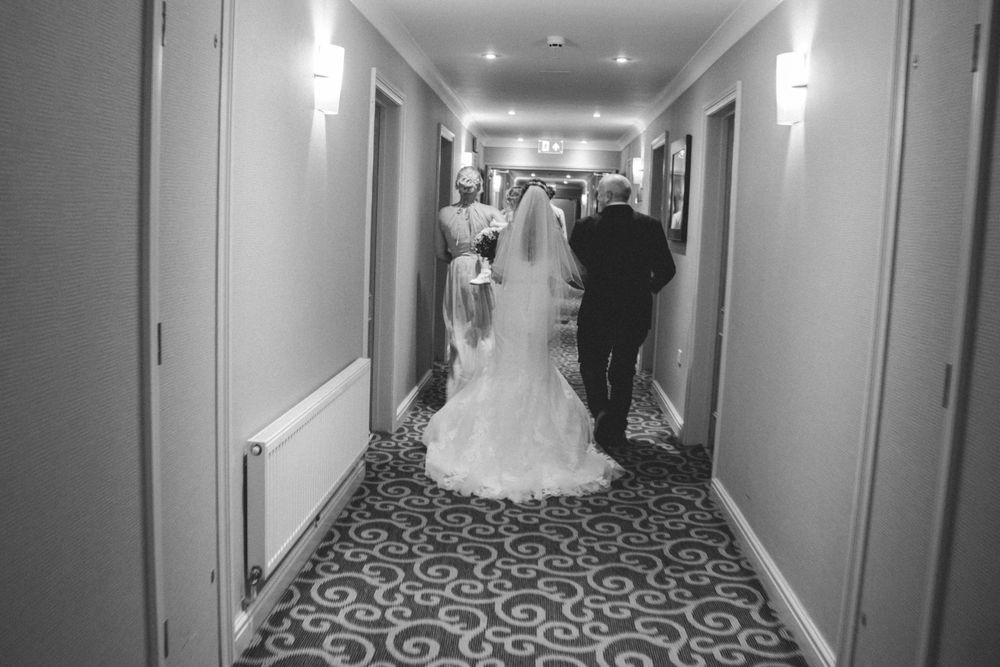Black and white photo of bride and groom walking down hotel hallway after ceremony.