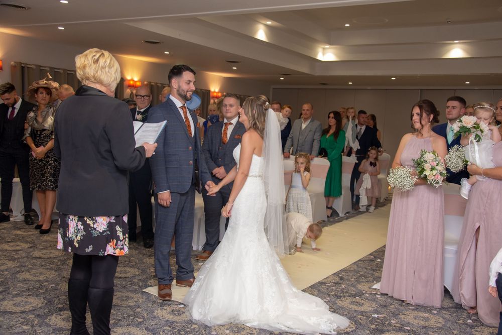 Wedding ceremony in progress with guests in formal attire watching from sides.