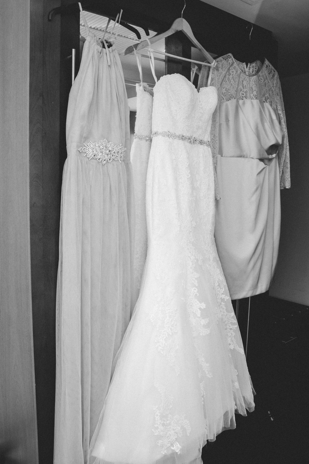 Three elegant white wedding dresses hanging on display in black and white photography.