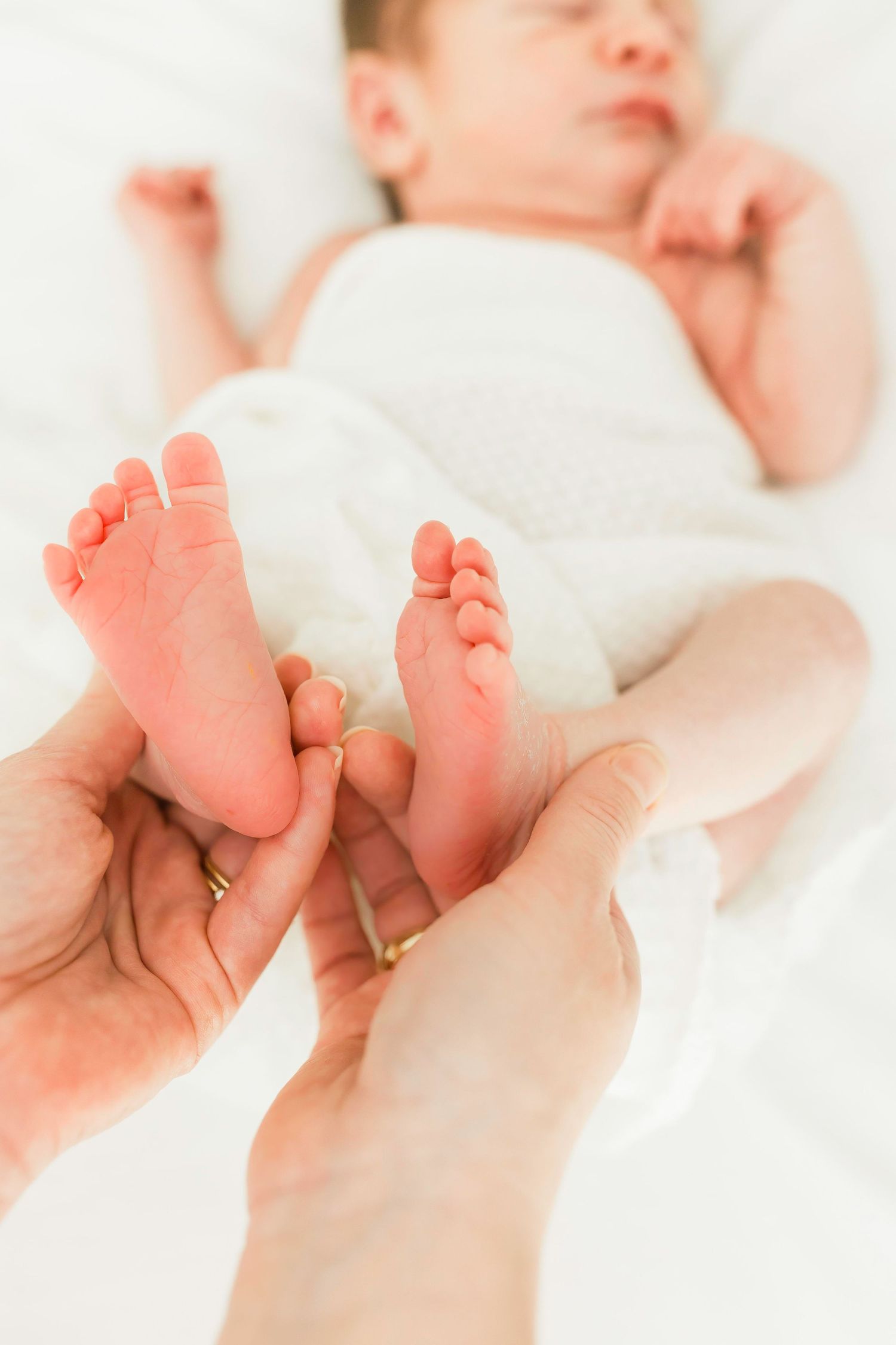 Tiny newborn baby feet being gently held in adult hands.