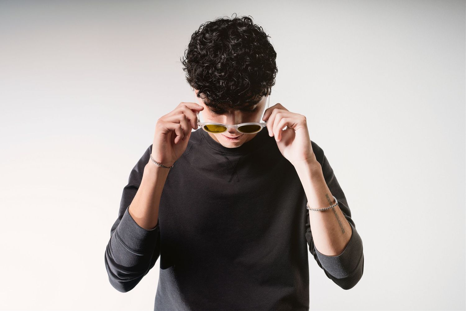 Minimalist portrait against white background showing person adjusting sunglasses.