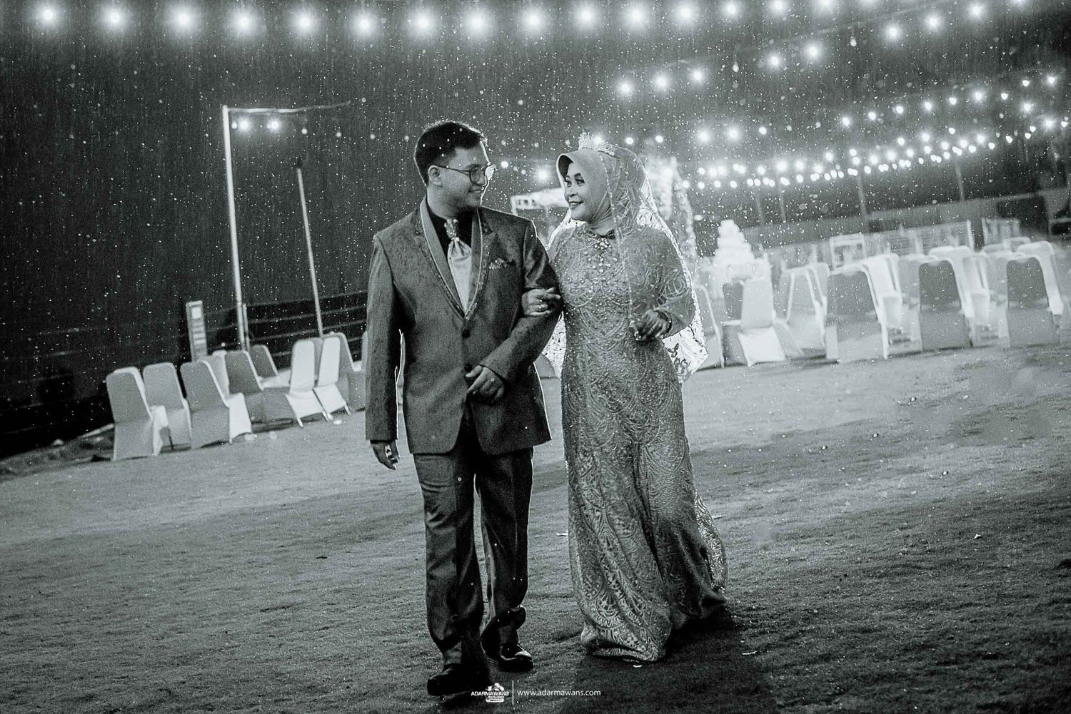 Couple walking at night under string lights in an outdoor venue.