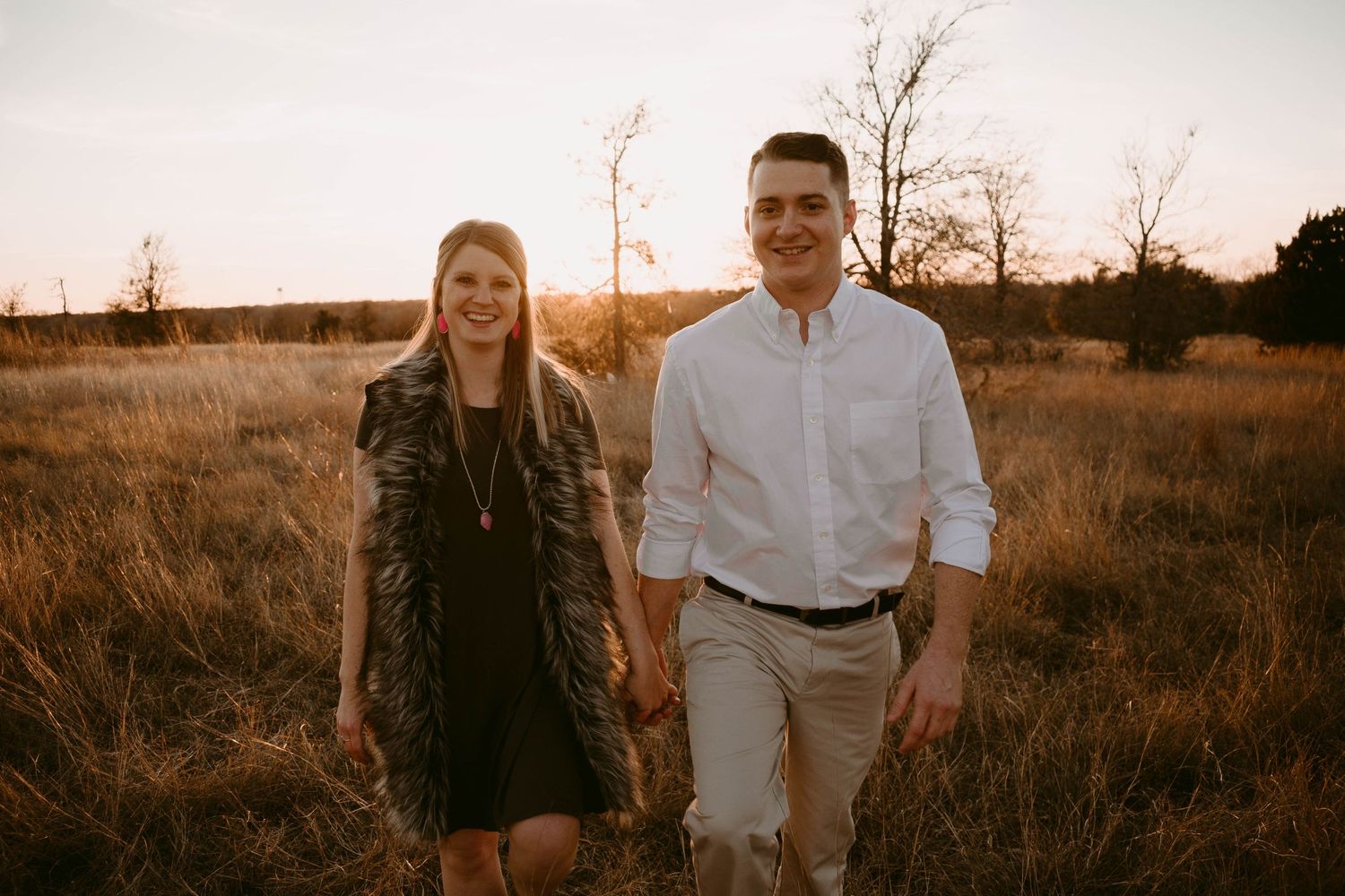 A couple takes a walk together through a rustic field at golden hour.