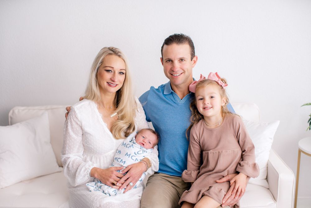 A family portrait in a bright studio setting featuring a newborn baby and soft neutral tones.