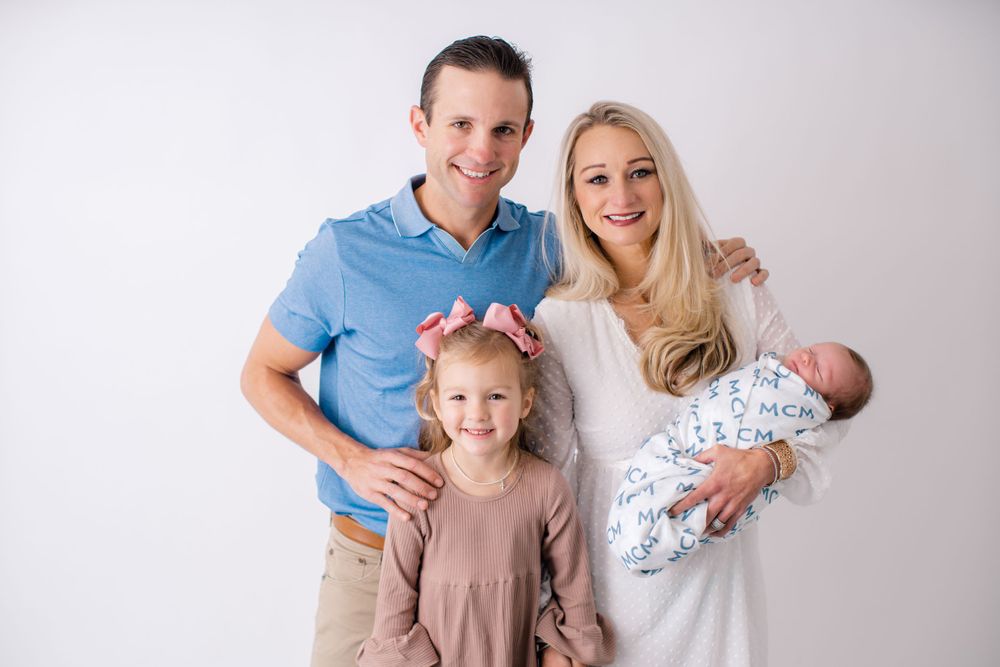 A studio family portrait with a newborn baby and toddler against a light background.