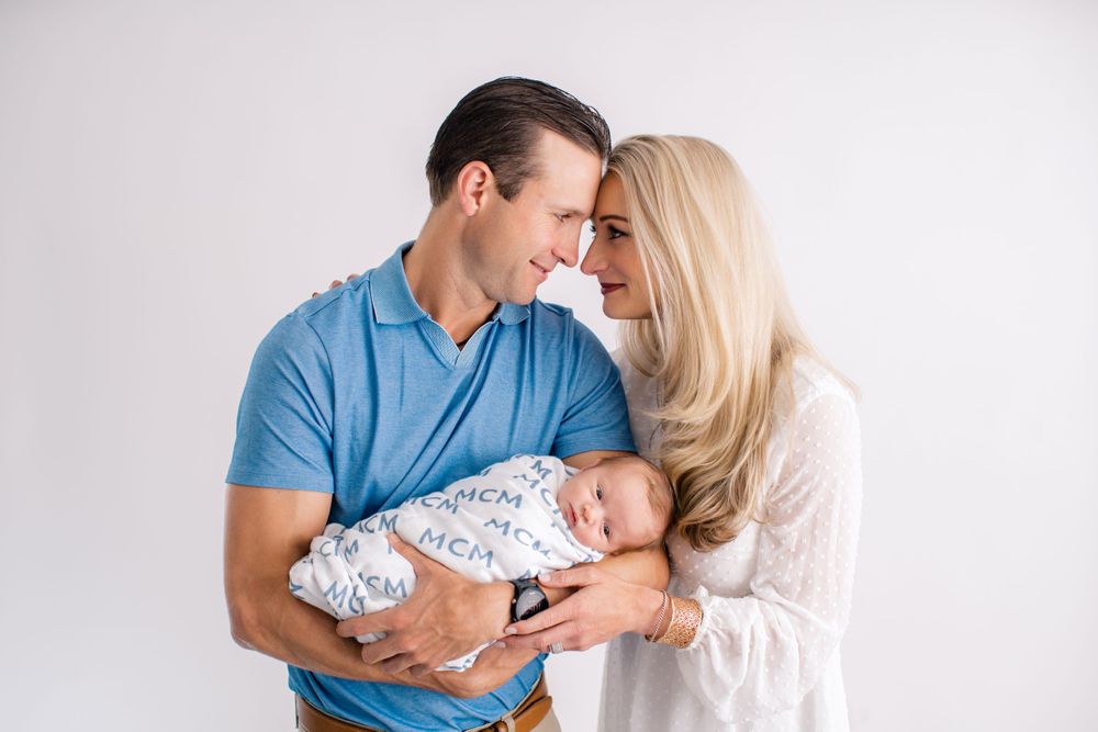 A sleeping newborn swaddled in a printed blanket is lovingly cradled during an intimate studio portrait session.