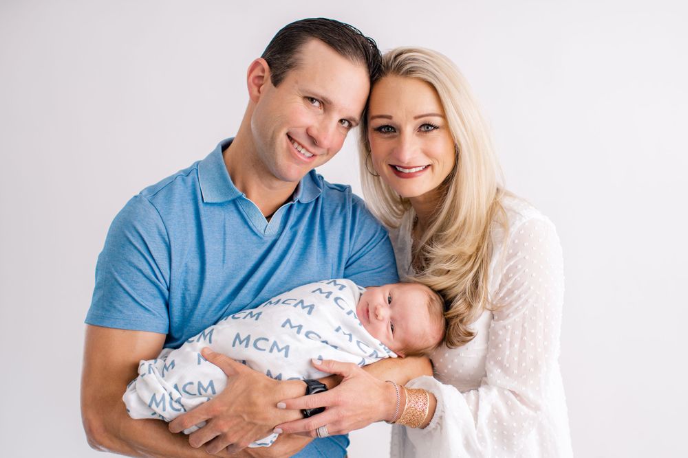 A newborn baby wrapped in a patterned blanket is held tenderly during a professional studio family photoshoot.