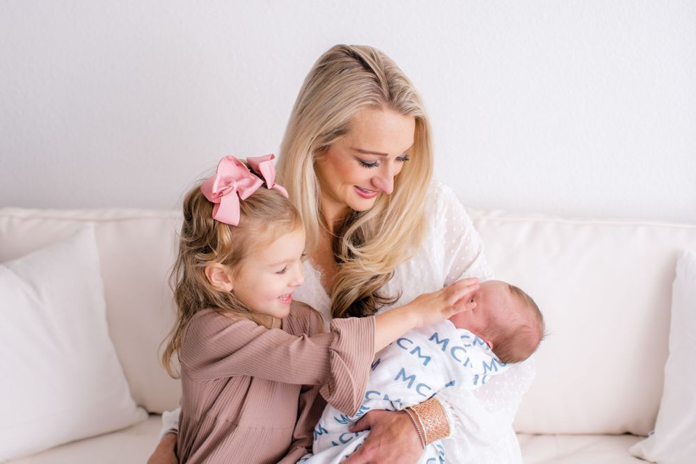 Family moment on white couch as mother and daughter bond with new baby.