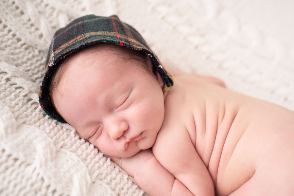 Peaceful sleeping newborn wearing plaid cap on white textured blanket.