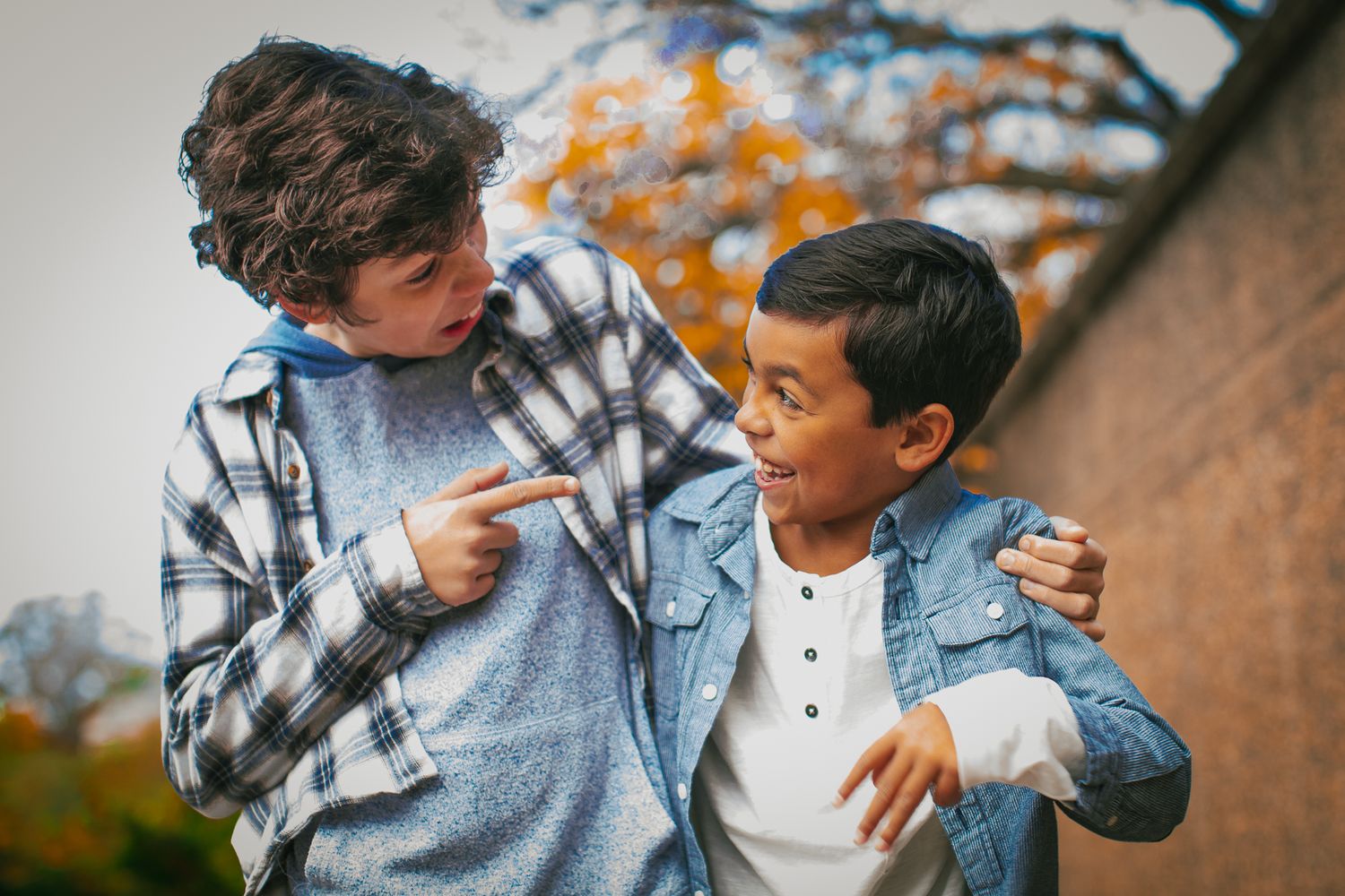 Two people playfully interacting outdoors with autumn foliage in the background.