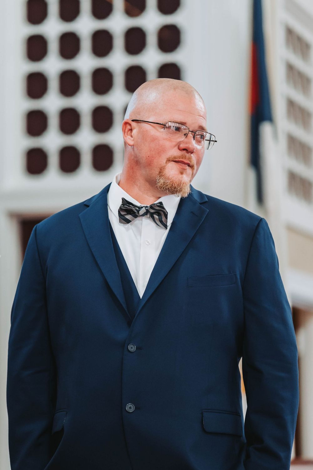 A groom in a navy blue suit with bow tie stands at attention during a wedding ceremony.