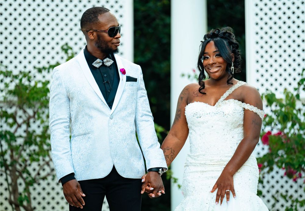 A newlywed couple poses together in front of a white lattice backdrop at their wedding celebration.