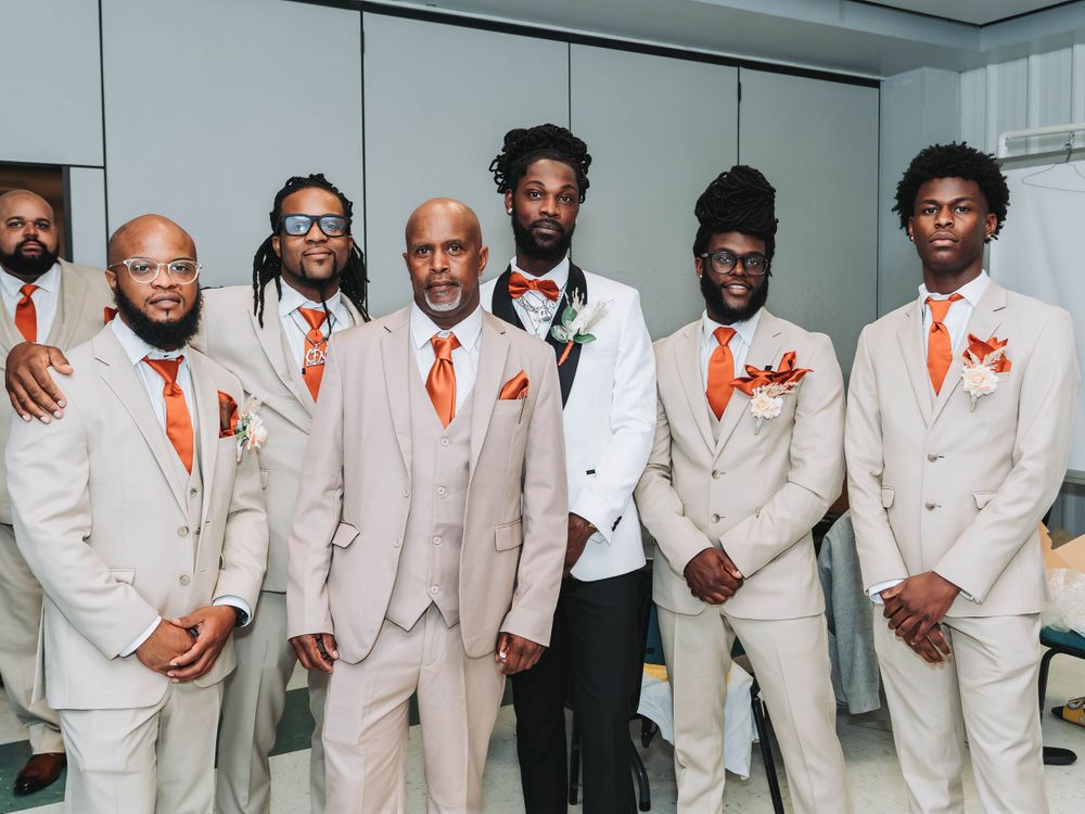 Groomsmen in beige suits with orange accessories pose together for a formal wedding photo.