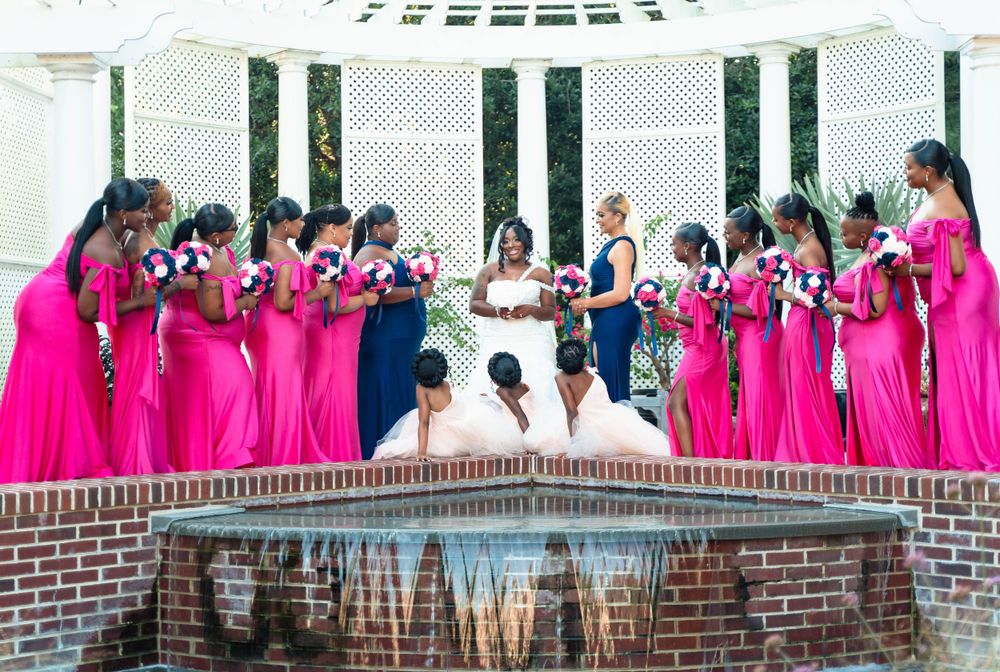 Wedding party in pink and blue attire gathered around reflecting pool with white columns.