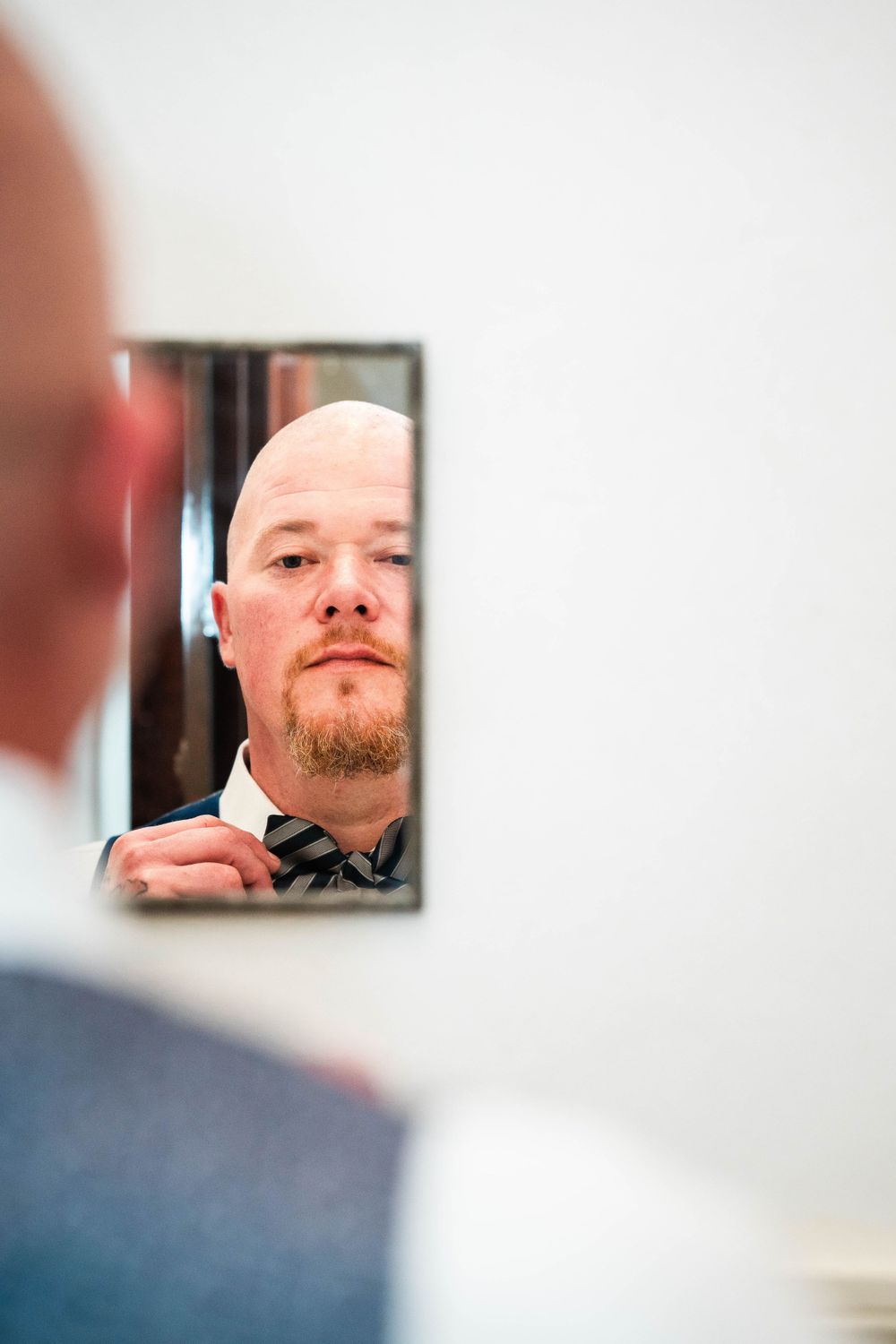 A close-up reflection in a mirror shows someone adjusting their bow tie before a formal event.