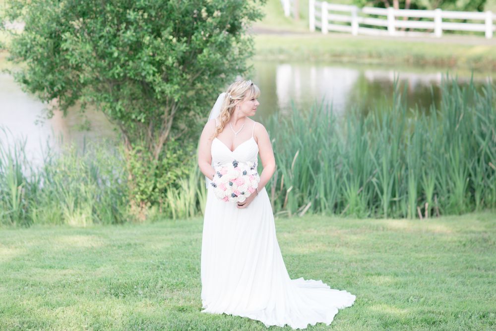Bridal portrait in flowing white gown beside pond with natural greenery.