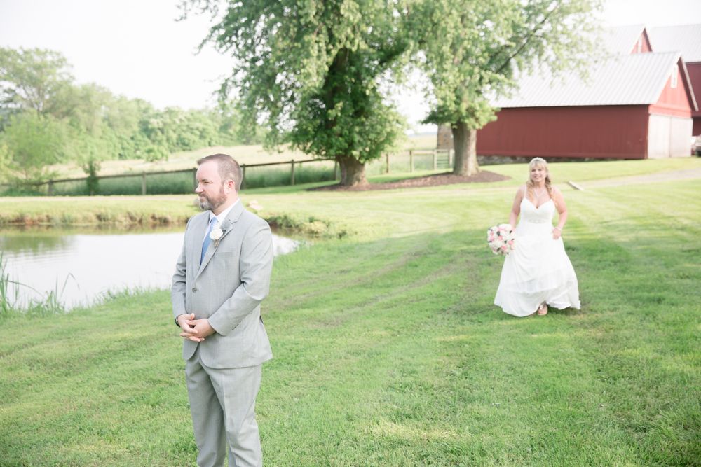 Wedding photo at rustic farm venue with pond and red barn in background.