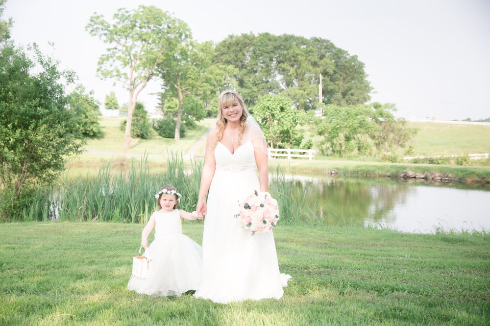 Wedding scene with matching white dresses against natural pond landscape.