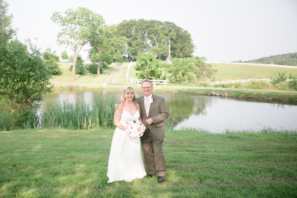Couple posing for wedding photos on grassy lawn with scenic pond backdrop.