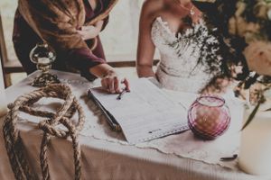 Bride signing wedding documents at decorated table during ceremony.