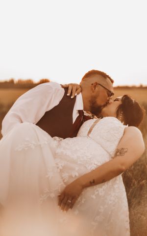 Groom lifting bride in a lace wedding gown for a romantic kiss in a golden field.