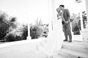 Black and white photo of bride and groom sharing a kiss on steps surrounded by tropical foliage.