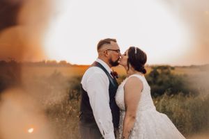 Bride and groom sharing a romantic kiss during a stunning golden sunset in an open field.
