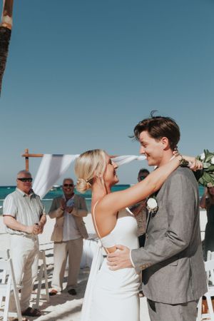 Bride and groom sharing first dance at outdoor beach wedding ceremony with guests applauding behind them.