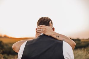 Bride placing tattooed hand on grooms neck during golden sunset in an open field.