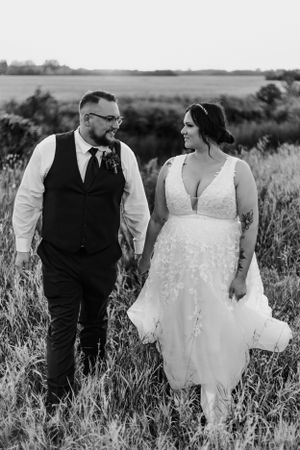 Bride and groom walking hand in hand through a field in elegant wedding attire, black and white.