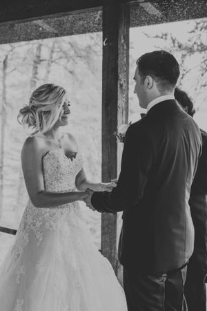 Bride and groom holding hands during wedding ceremony in black and white.