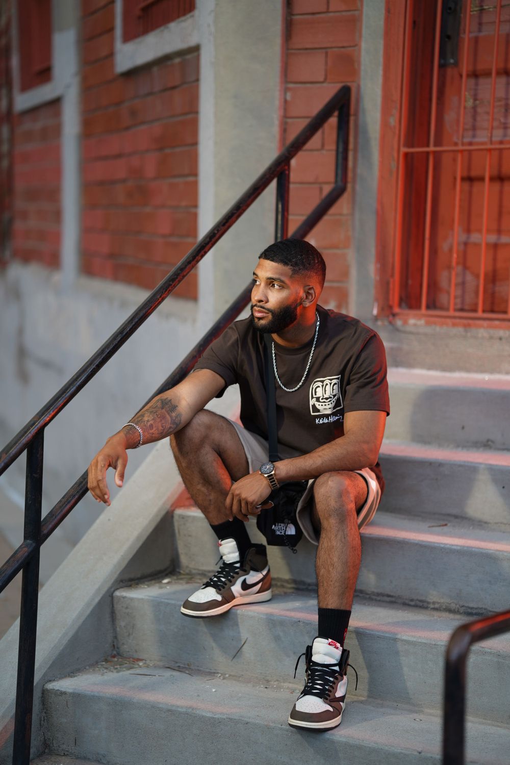 Person sitting on concrete steps wearing casual streetwear and Nike sneakers in an urban setting.